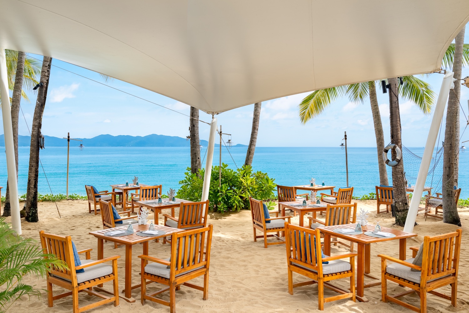 Tables du Beach House sur la plage du Santiburi entre les cocotiers face à la mer